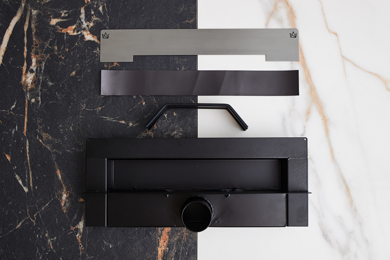 Elementy zestawu odpływu ściennego WALL PRO Brushed Graphite na tle jasnej i ciemnej płytki