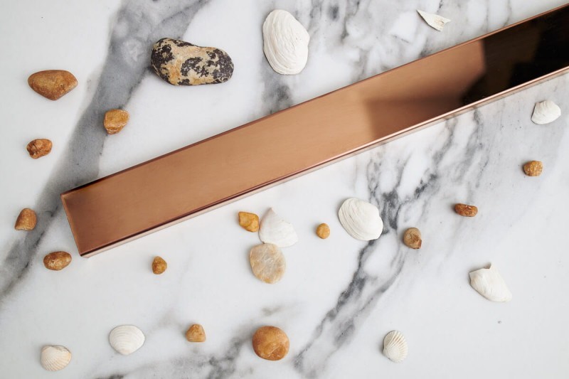 Odpływ liniowy przyścienny różowe złoto na tle jasnej płytki.