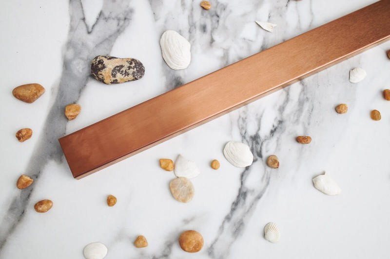 Odpływ przyścienny różowe złoto na tle jasnej płytki.