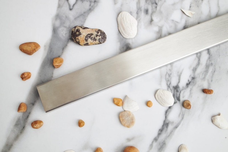 Odpływ liniowy przyścienny stalowy na tle jasnej płytki.