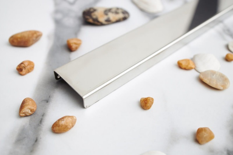 Odpływ przyścienny stalowy błyszczący na tle jasnej płytki.