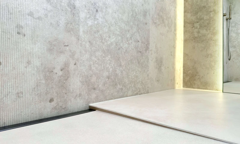 Grafitowy odpływ liniowy przyścienny zamontowany w łazience z jednospadowym spadkiem.