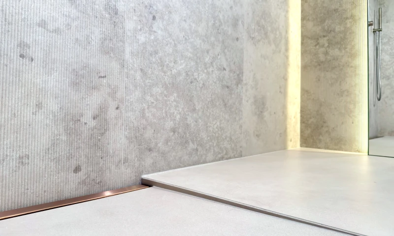 Przyścienny odpływ liniowy różowe złoto zamontowany na pełną szerokość prysznica