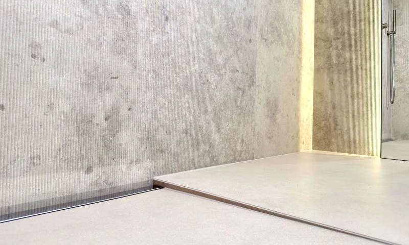 Stalowy odpływ przyścienny na pełna szerokość zamontowany w łazience.