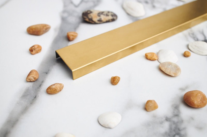 Maskownice dekoracyjna złotego odpływu łazienkowego w wykończeniu szczotkowanym na tle białego kafelka