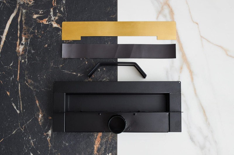 Rozłożone elementy złotego odpływu ściennego WALL PRO na tle jasnej i ciemnej płytki